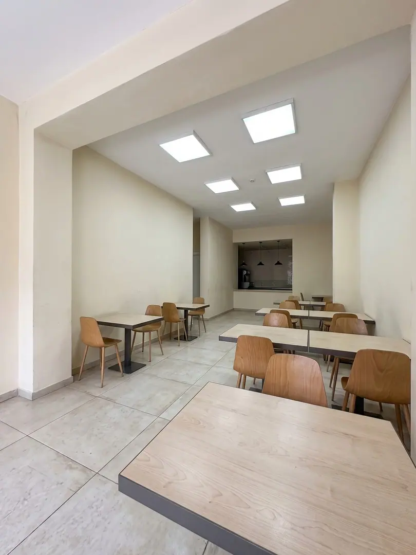 Simulazione con AI del locale prima del progetto, con pareti intonacate color crema, plafoniere quadrate e tavoli semplici con sedie in legno